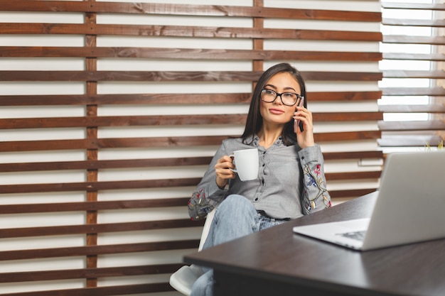 Mujer sonriente feliz que trabaja con el ordenador portátil y que bebe café