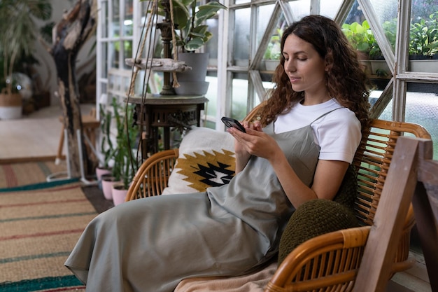 Una mujer sonriente feliz se relaja en el jardín de su casa usando un teléfono inteligente chateando en las redes sociales con un amigo