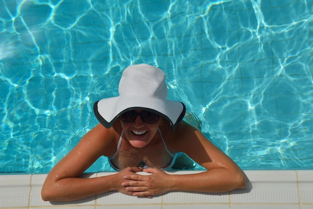 Mujer sonriente feliz con sombrero y gafas de sol en la piscina en el resort tropical