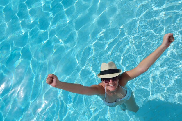 Mujer sonriente feliz con sombrero y gafas de sol en la piscina en el resort tropical