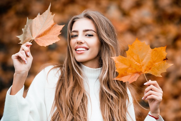 Mujer sonriente feliz sosteniendo en sus manos hojas de arce amarillas sobre fondo de otoño