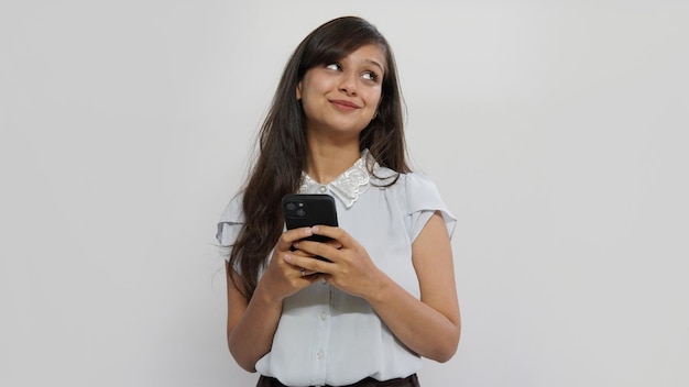 Una mujer sonriente feliz sostiene su teléfono sobre un fondo de pared gris. Mirando a un lado.