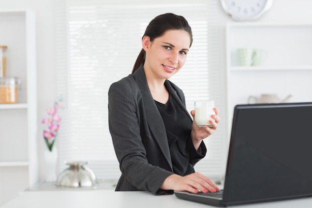 Mujer sonriente frente a la computadora portátil con vaso de leche