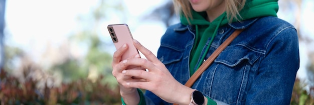 Mujer sonriente con gafas de sol que mira el teléfono inteligente en la calle recibe un mensaje de notificación y