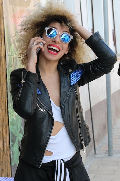 Foto mujer sonriente con gafas de sol tomando el teléfono móvil al aire libre