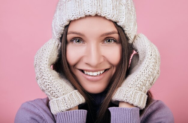 Mujer sonriente en un gorro de punto de invierno con las manos en guantes cerca de la cabeza