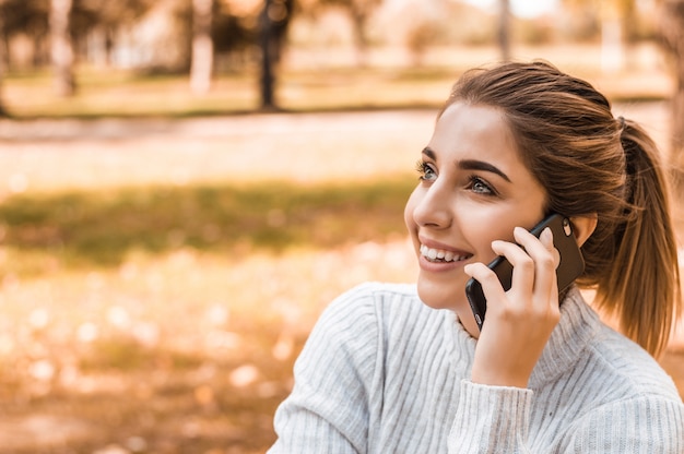 Mujer sonriente hermosa joven que habla en el teléfono celular en parque.