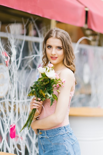 Mujer sonriente hermosa joven en ropa de verano de moda. Una sexy mujer despreocupada posa con el telón de fondo de la calle con un ramo de rosas. Modelo de exterior positivo