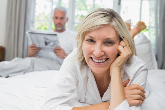 Mujer sonriente con hombre leyendo el periódico en la cama