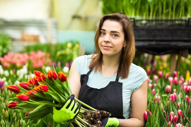 Mujer sonriente jardinero florista sosteniendo un ramo de flores de pie en un invernadero donde se cultivan los tulipanes