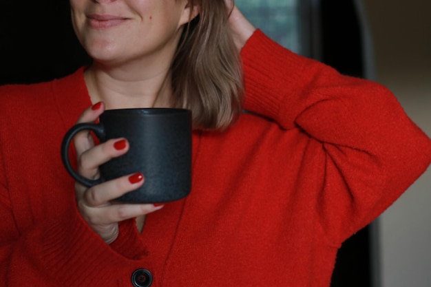 mujer sonriente con jersey rojo sosteniendo una taza de café gris