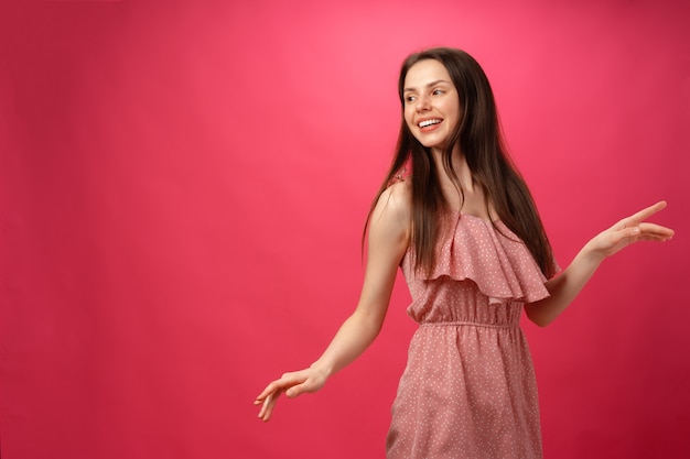 Mujer sonriente joven bailando con los brazos extendidos contra el fondo de color rosa