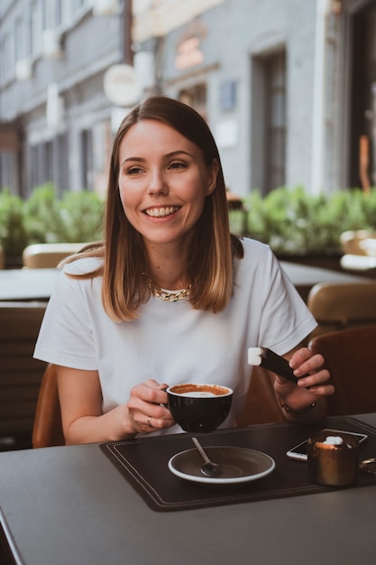 Mujer sonriente joven bebe café en un café de la calle