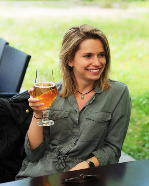 Mujer sonriente joven bebiendo un vaso de cerveza en un restaurante de la calle