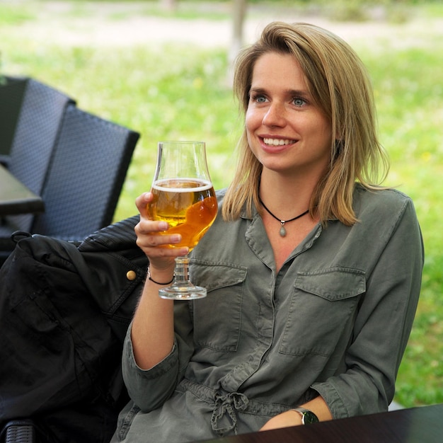 Mujer sonriente joven bebiendo un vaso de cerveza en un restaurante de la calle