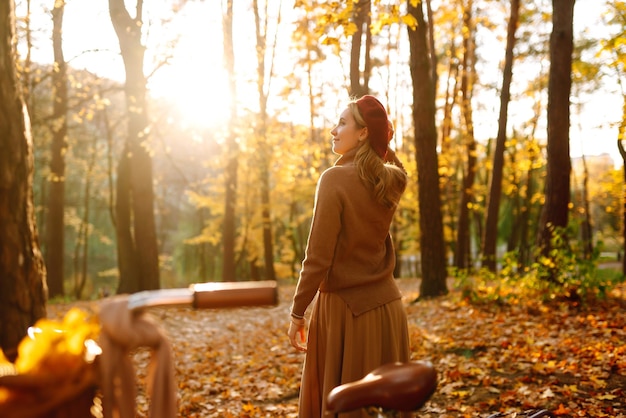 Mujer sonriente joven con una bicicleta camina en el bosque de otoño al atardecer