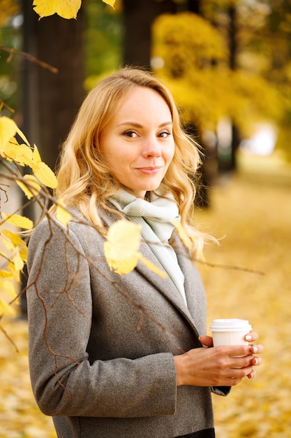 Mujer sonriente joven con café al aire libre en un soleado día de otoño retrato en primer plano mirando a la cámara