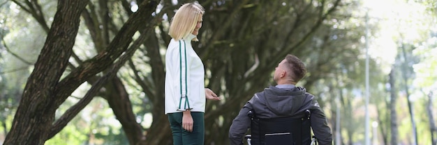 Mujer sonriente joven camina en el parque con el hombre en silla de ruedas amistad y apoyo de personas con