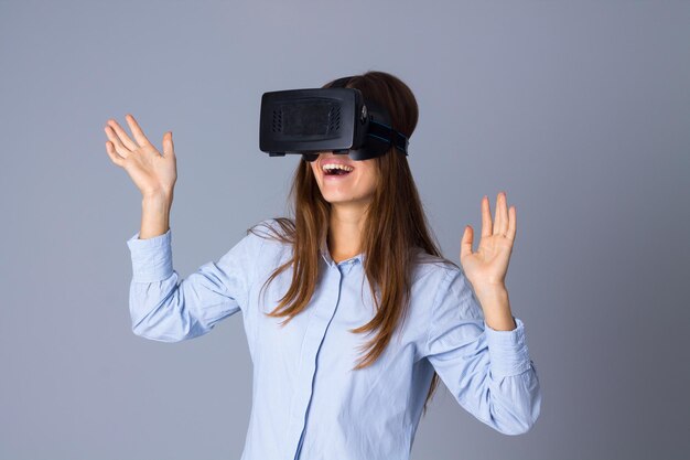 Mujer sonriente joven en camisa azul con gafas de realidad virtual sobre fondo gris en estudio