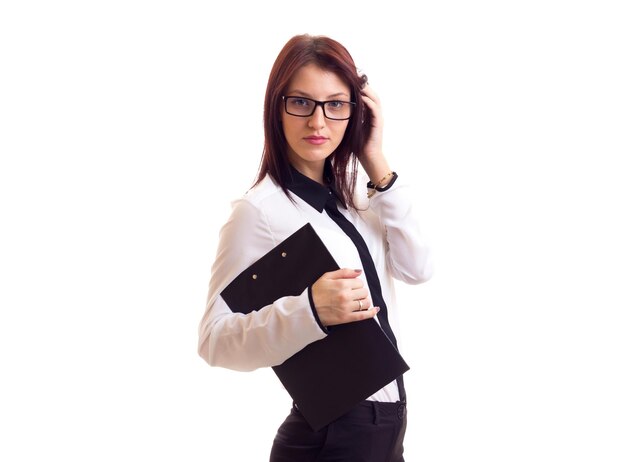 Mujer sonriente joven en camisa blanca y pantalones con pelo largo y oscuro y gafas sosteniendo una carpeta