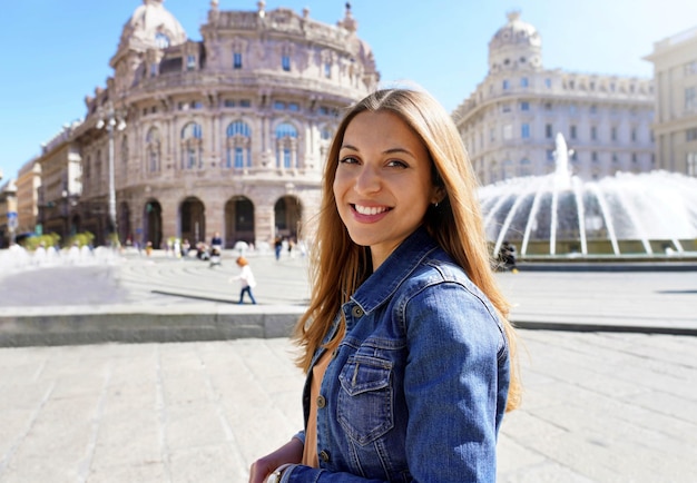 Mujer sonriente joven con chaqueta de mezclilla azul en la ciudad histórica mirando a la cámara