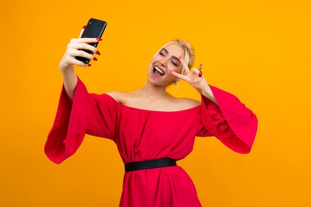 Mujer sonriente joven con un elegante vestido rojo hace una foto de sí misma en el teléfono en un estudio amarillo