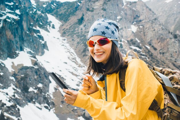 Mujer sonriente joven escribiendo un mensaje en el teléfono inteligente en las montañas rocosas nevadas