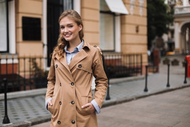 Mujer sonriente joven en gabardina con alegría