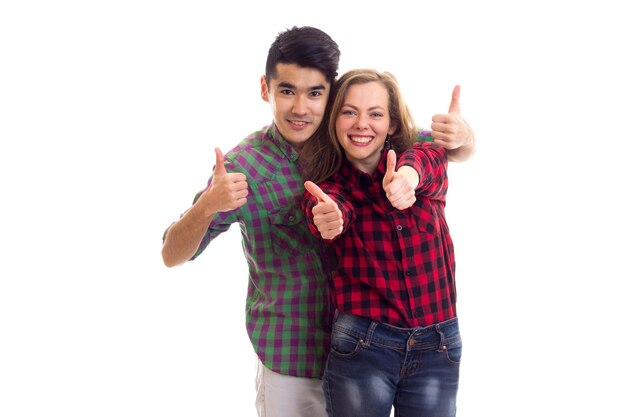 Mujer sonriente joven con un hombre joven de aspecto inteligente con cabello oscuro en camisas a cuadros que muestran los pulgares hacia arriba