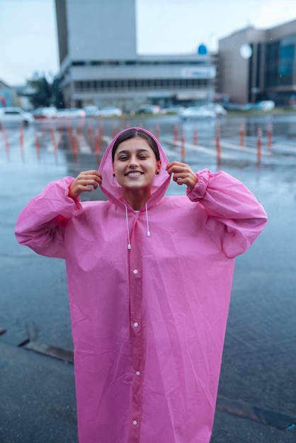 Mujer sonriente joven en un impermeable rosa disfrutando de un día lluvioso