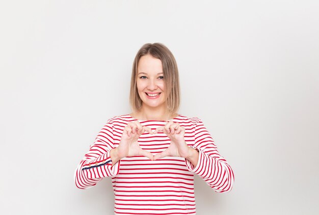 La mujer sonriente joven muestra el signo de la mano del corazón.