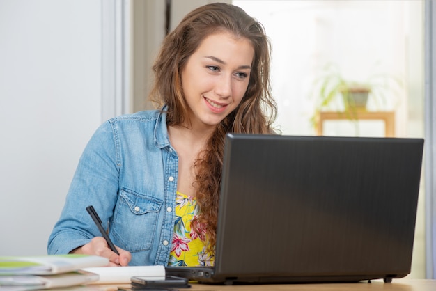 La mujer sonriente joven con el pelo largo está utilizando una computadora portátil