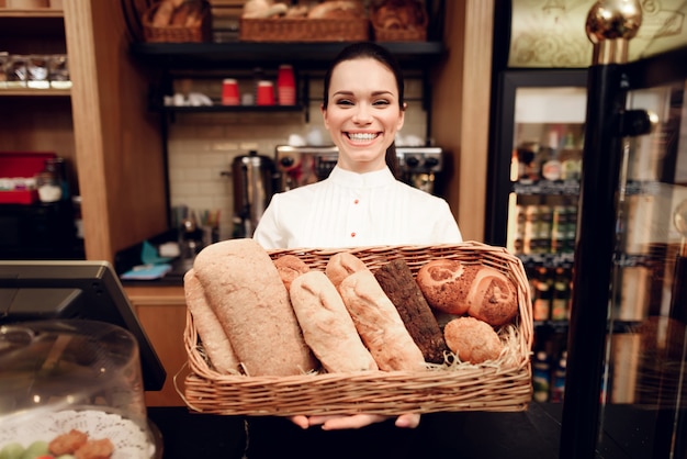 Mujer sonriente joven que se coloca con pan en panadería.