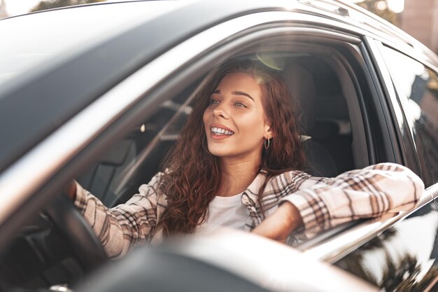 Mujer sonriente joven que conduce un coche en la ciudad