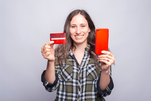 Foto mujer sonriente joven que muestra la tarjeta de crédito roja y el teléfono inteligente.