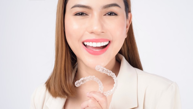 Mujer sonriente joven que sostiene los apoyos invisalign en el estudio, la salud dental y el concepto de ortodoncia