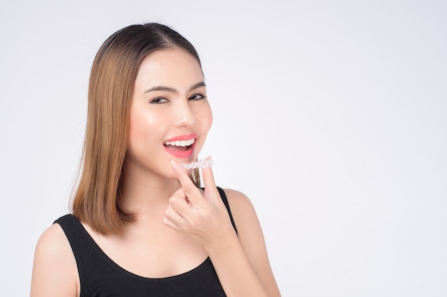 Mujer sonriente joven que sostiene los apoyos invisalign en el estudio, la salud dental y el concepto de ortodoncia