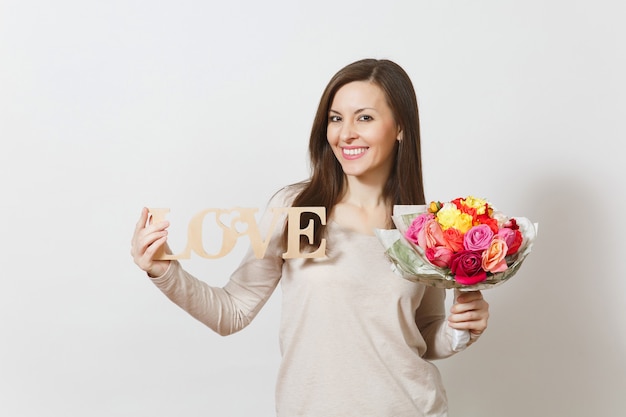 Mujer sonriente joven que sostiene la palabra de madera Amor, ramo de flores rosas hermosas aisladas sobre fondo blanco. Copie el espacio para publicidad. Concepto de día de San Valentín o día internacional de la mujer.