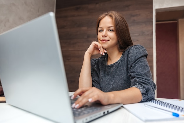 Mujer sonriente joven que trabaja en la computadora portátil en casa