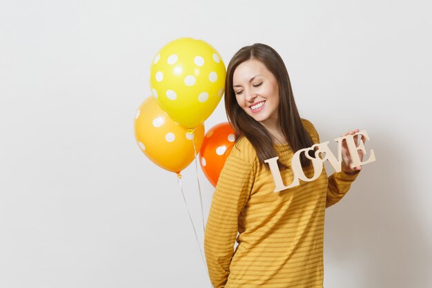 Mujer sonriente joven romántica hermosa que sostiene la palabra de madera amor, globos de aire de color amarillo anaranjado sobre fondo blanco. Copie el espacio para publicidad. Concepto de día de San Valentín o día internacional de la mujer.