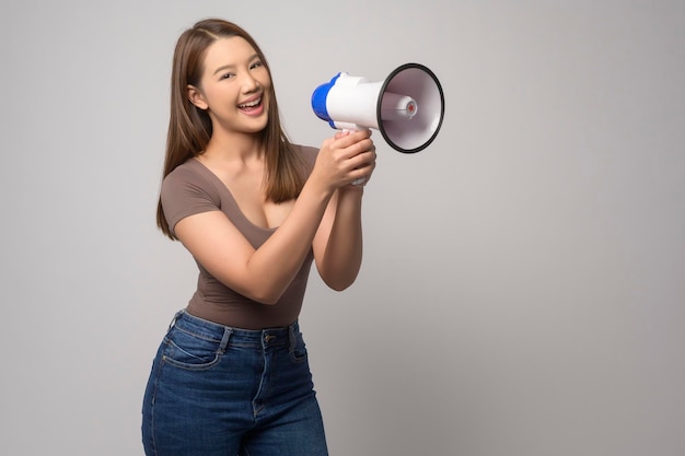 Mujer sonriente joven sosteniendo megáfono sobre fondo blanco studiox9