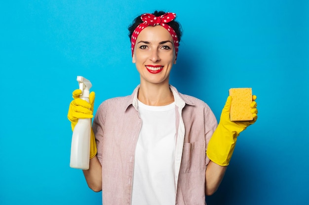 Mujer sonriente joven sosteniendo spray y esponja sobre fondo azul.