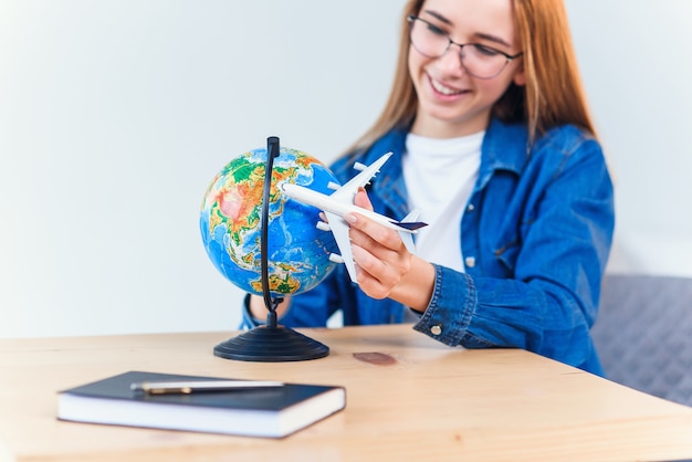 La mujer sonriente joven sostiene el modelo disponible del aeroplano. Feliz hermosa chica planeando viaje de vacaciones.