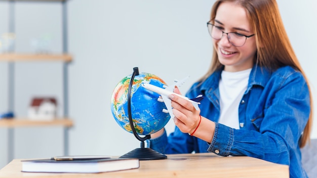 La mujer sonriente joven sostiene el modelo disponible del aeroplano. Feliz hermosa chica planeando viaje de vacaciones.