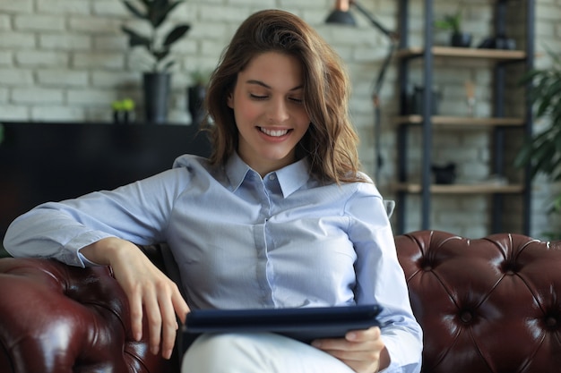 Mujer sonriente joven con tablet pc en el sofá.