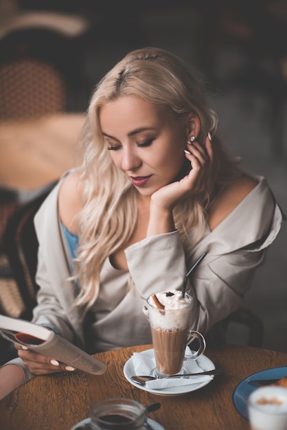 Mujer sonriente leyendo un libro de papel tomando café en la cafetería closeup