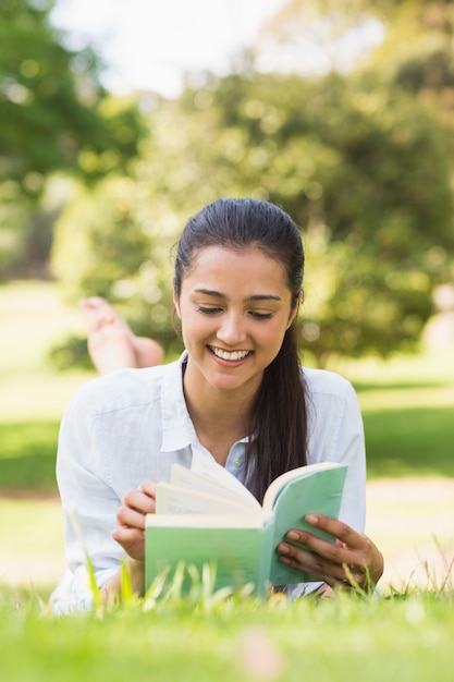 Mujer sonriente leyendo un libro en el parque