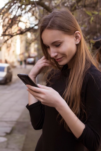 Mujer sonriente leyendo un mensaje de texto en un teléfono inteligente en la calle