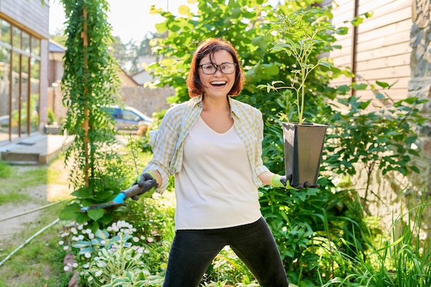 Mujer sonriente con maceta con planta de peonía y pala de jardín