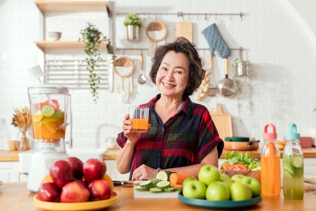 Mujer sonriente madura cocinar ensalada de frutas y verduras Atractiva mujer madura con ensalada de frutas verdes frescas en casa Delantal de mujer mayor de pie en el mostrador de la cocina relajándose en casa el fin de semana